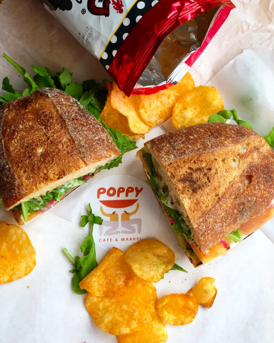 Two sandwich halves and potato chips on paper with a Poppy Cafe & Market sticker, seen from above
