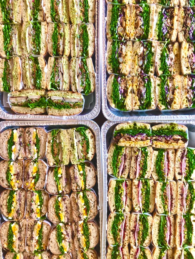 Foil trays of sandwich halves, with greens and colourful fillings facing up