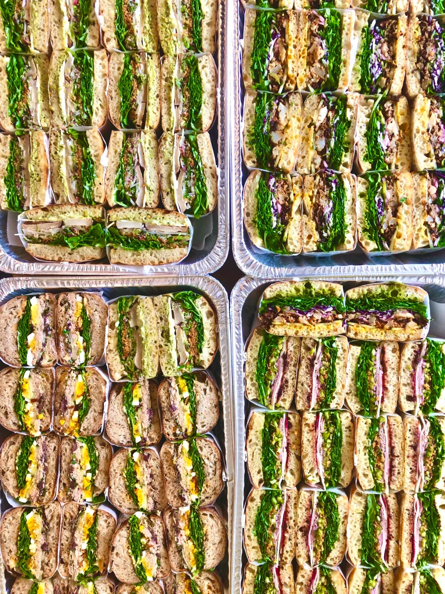 Four foil trays filled with sandwich halves, with greens and colourful fillings facing up