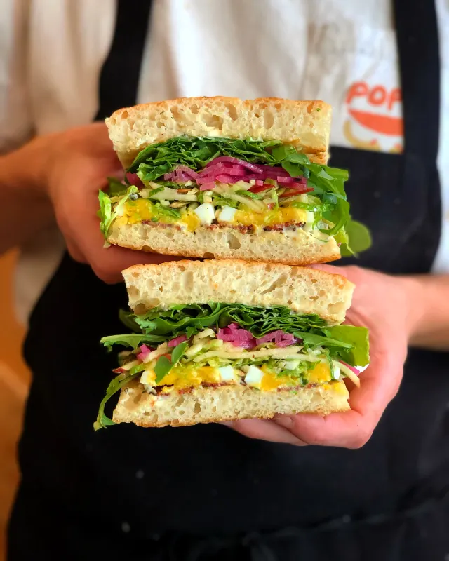 Two sandwich halves held up in two hands, a Poppy shirt behind