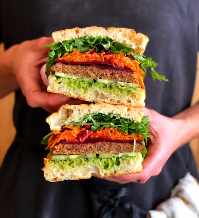 Two tall sandwich halves held out toward the camera in both hands
