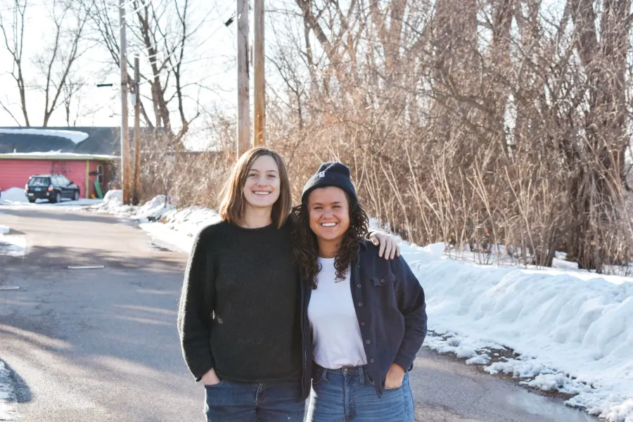 Two people standing arm in arm on a snowy roadside
